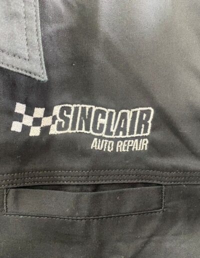 Close-up of a black fabric with "Sinclair Auto Repair" and a checkered flag pattern embroidered in white thread.