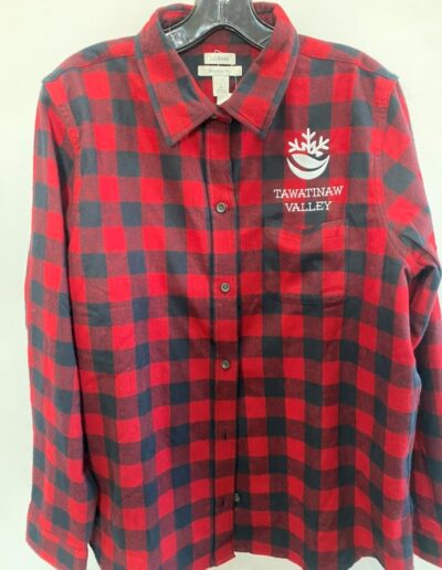 Red and black checkered flannel shirt with "TAWATINAW VALLEY" and a logo embroidered on the left chest, hanging on a black hanger.