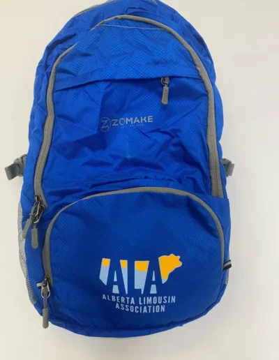 Blue backpack with gray zippers, featuring "Zomake" logo on top and "Alberta Limousin Association" with a yellow cow silhouette on the front pocket.